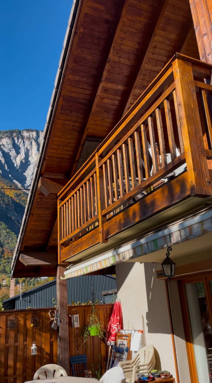Balcon de chalet fraîchement lasuré avec les falaises de l'Oisans en arrière-plan