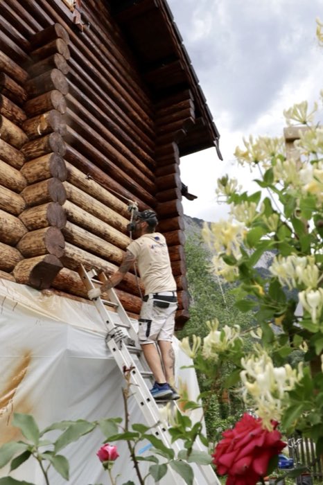 Application de lasure au pistolet sur la façade en rondins d'un chalet